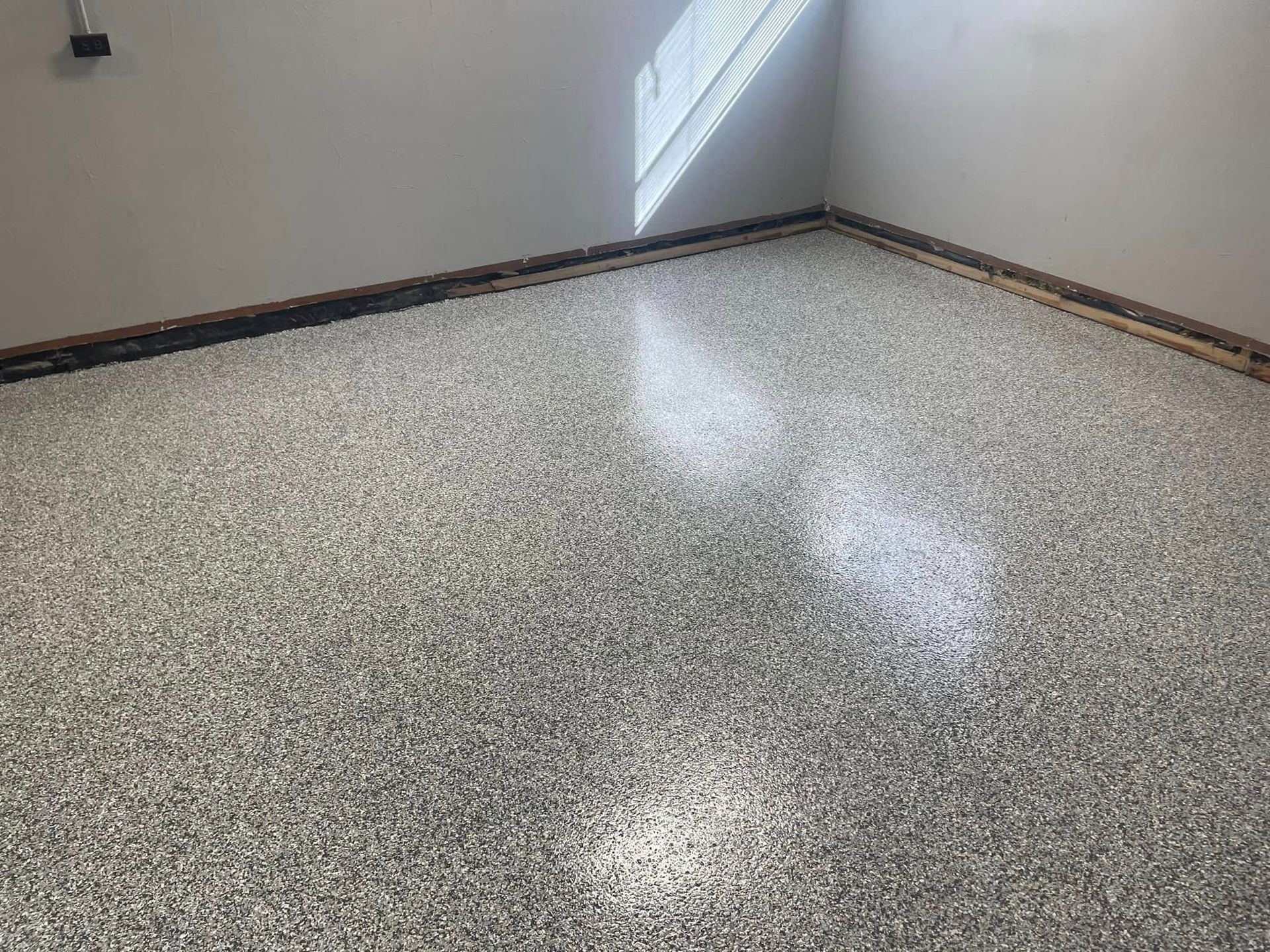 Epoxy-coated garage floor with gray and white chips. Walls are light gray, window at upper right.