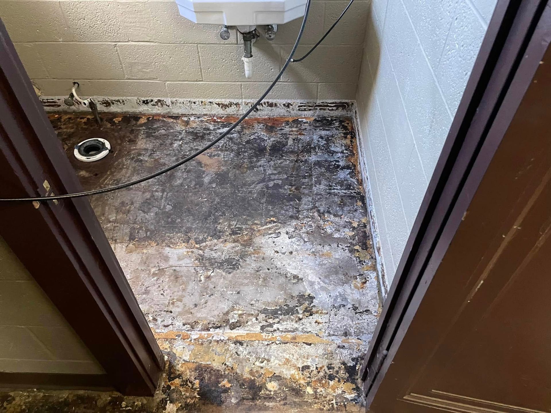 Bathroom floor, damaged and stained with a toilet and doorway visible.