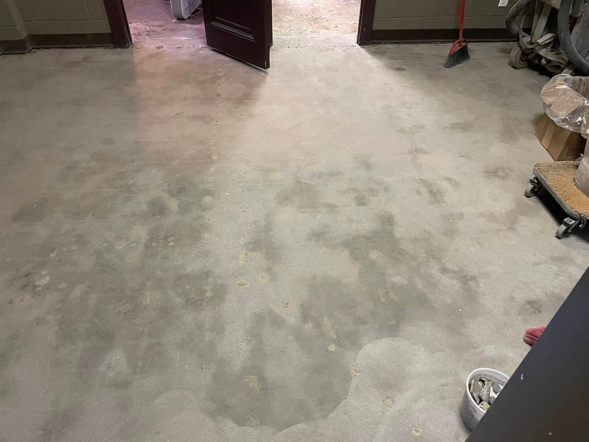 Concrete floor in a room. A door is open, with a broom and other items present.