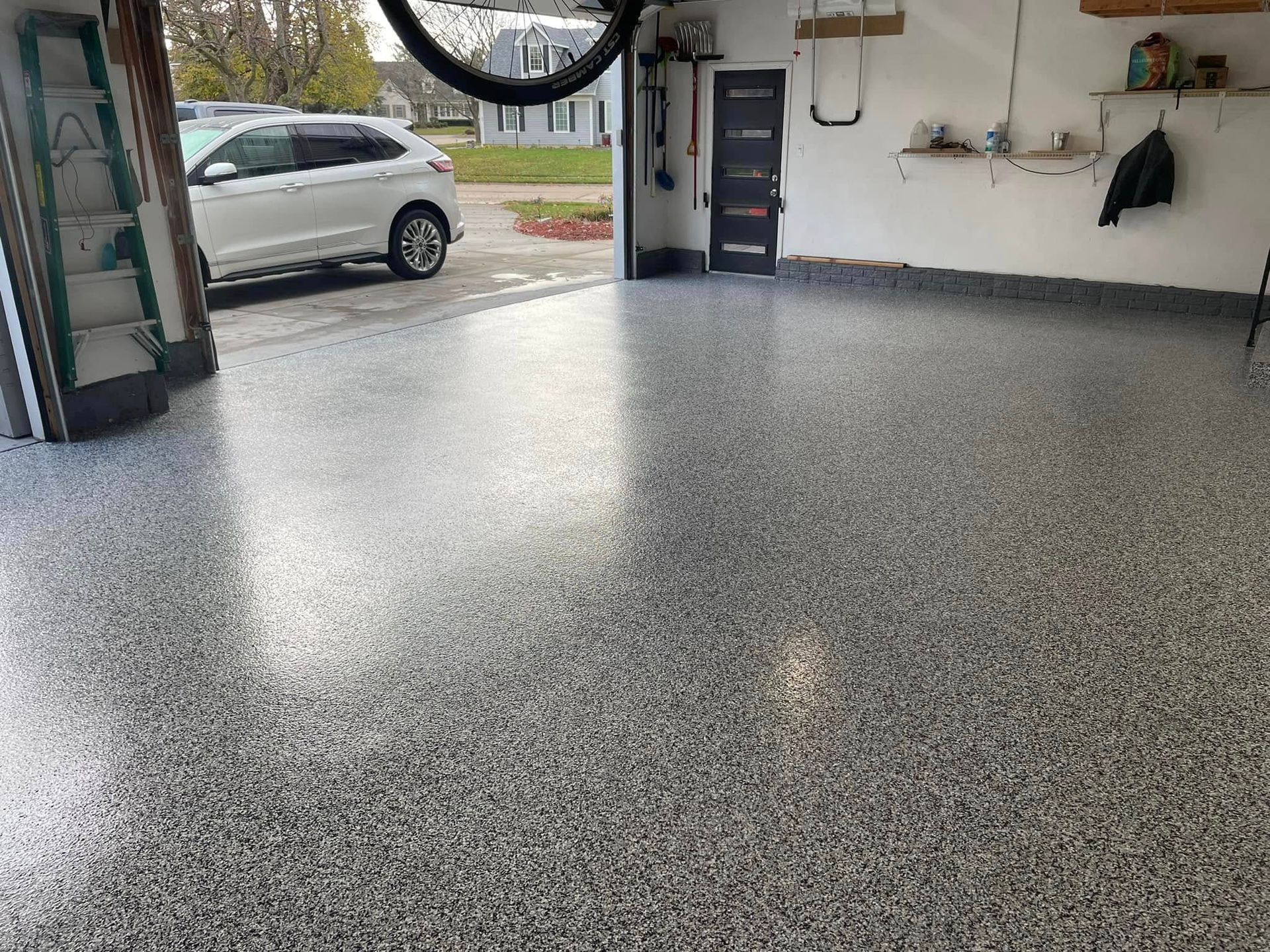 Garage with a shiny, speckled epoxy floor; a car is parked outside.