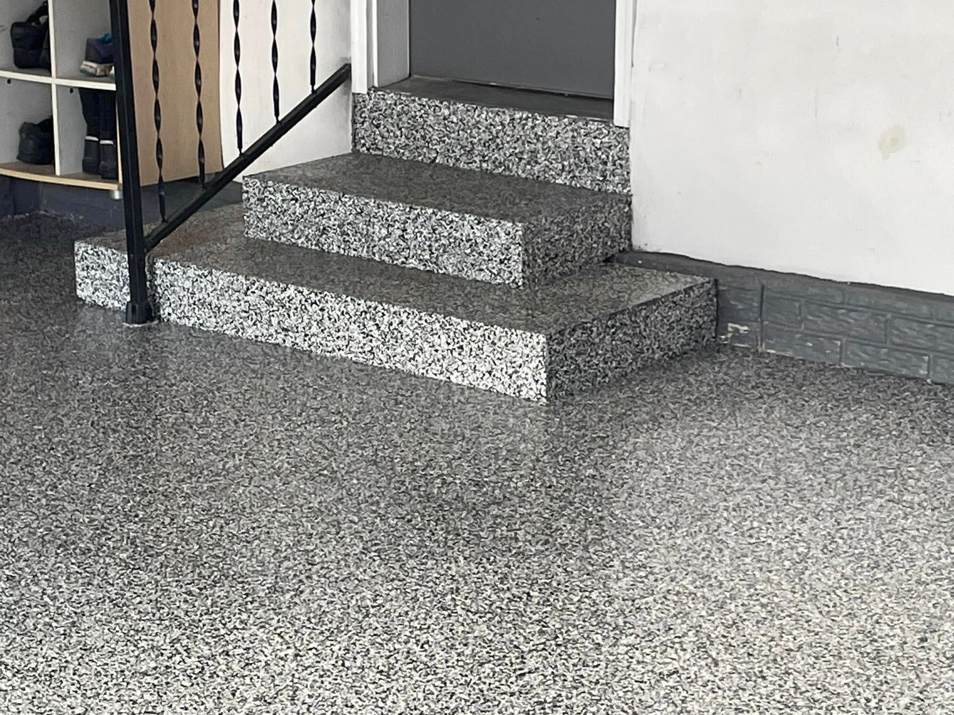Gray speckled epoxy floor and steps leading into a garage, with a black handrail.