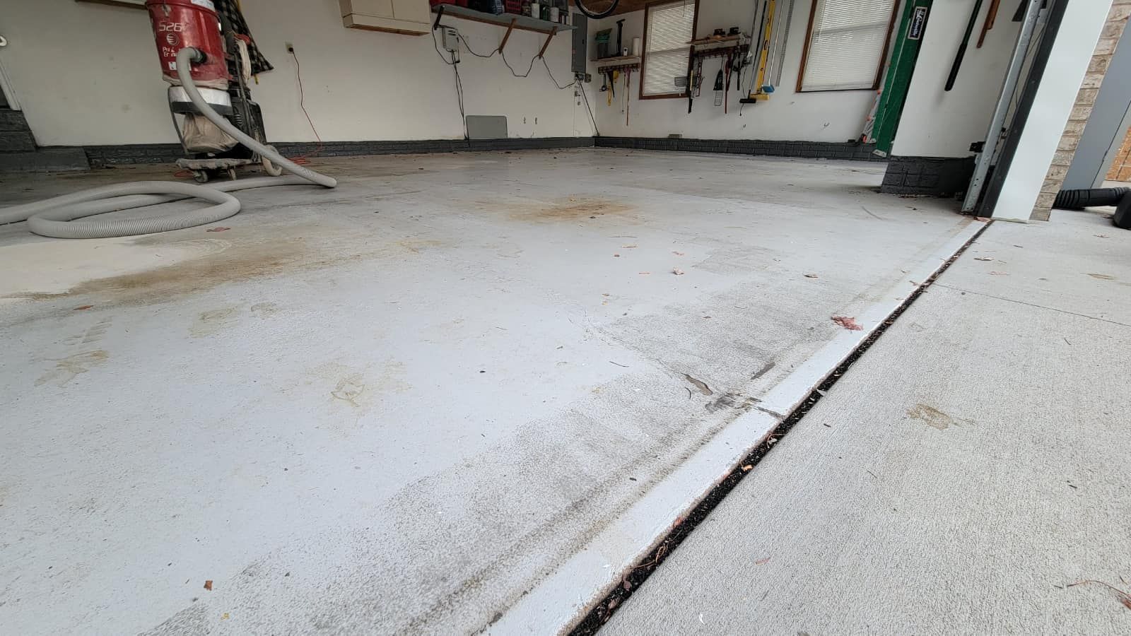 Garage interior with a gray painted floor showing stains and a crack. A hose and door are visible.