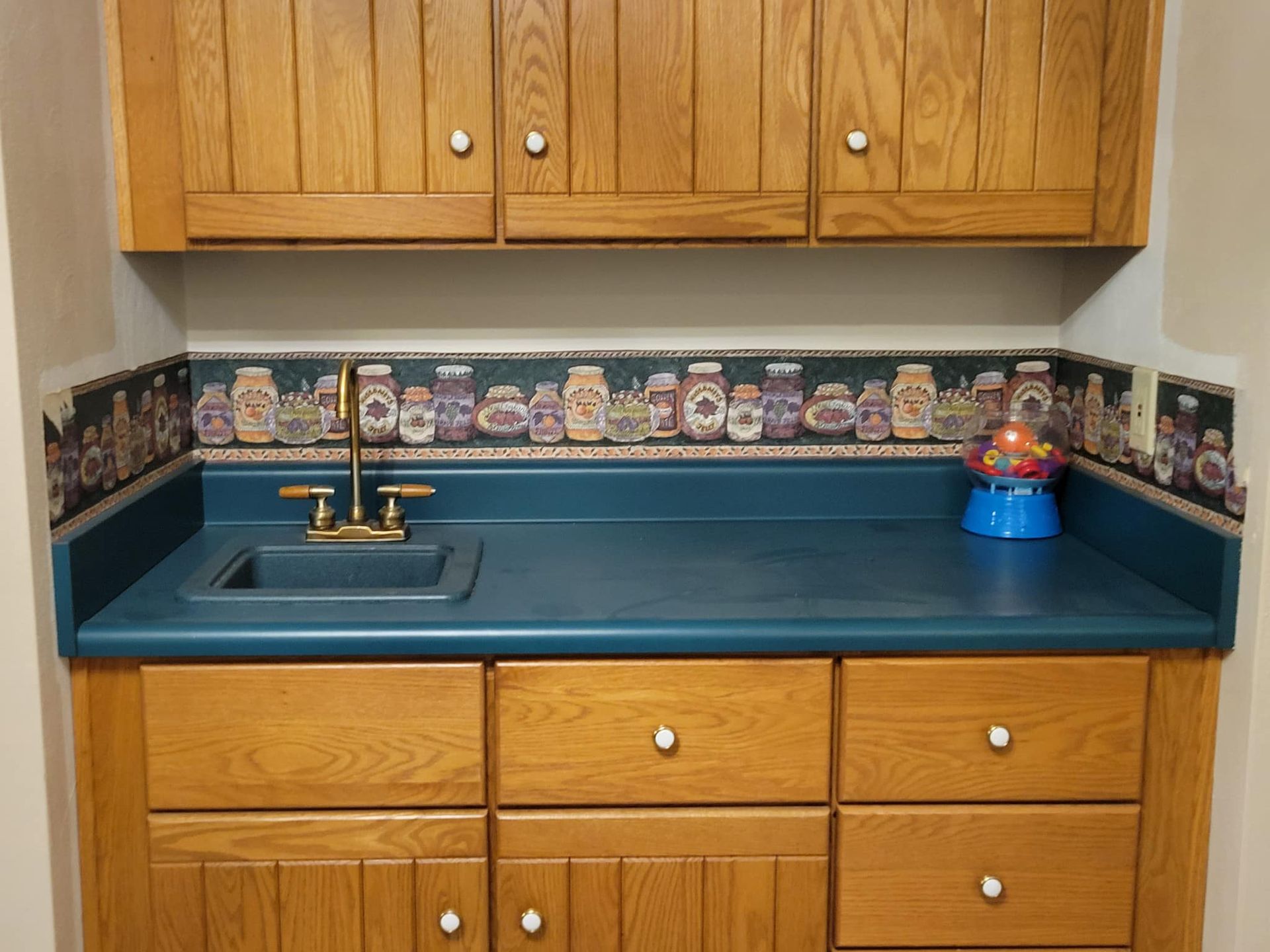 Oak cabinets with a blue countertop, sink, and decorative jars wallpaper border.