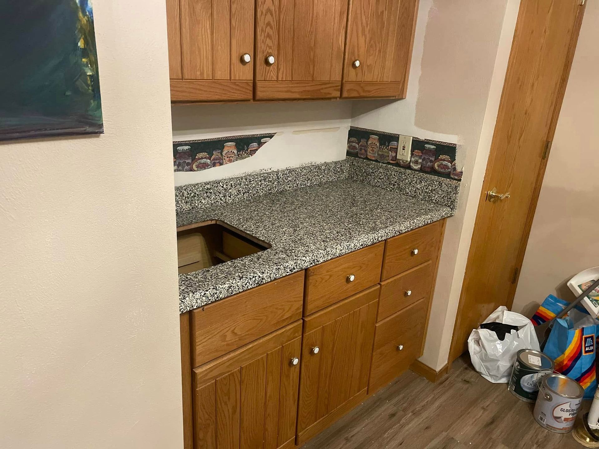 Oak cabinets with granite countertop, sink, and city-themed backsplash in a room with a wooden door.