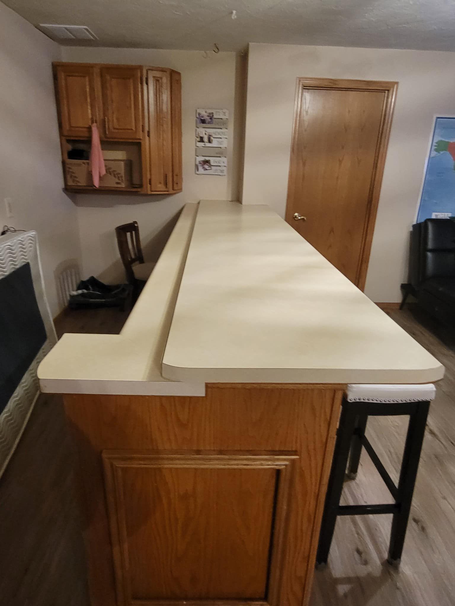 Wooden bar with light countertop, cabinets, door, and a barstool.