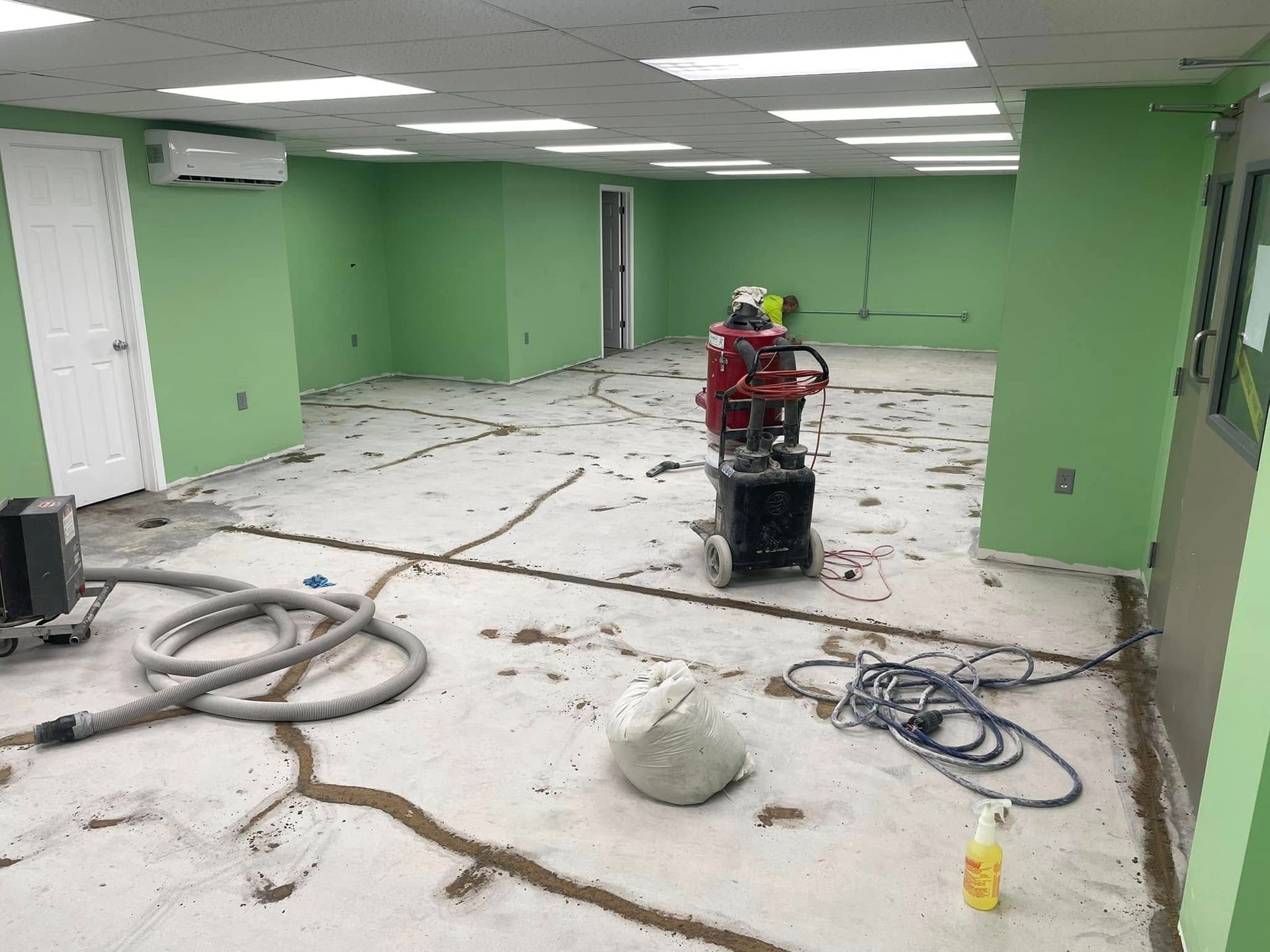 Interior construction site with green walls, cracked concrete floor, and equipment.