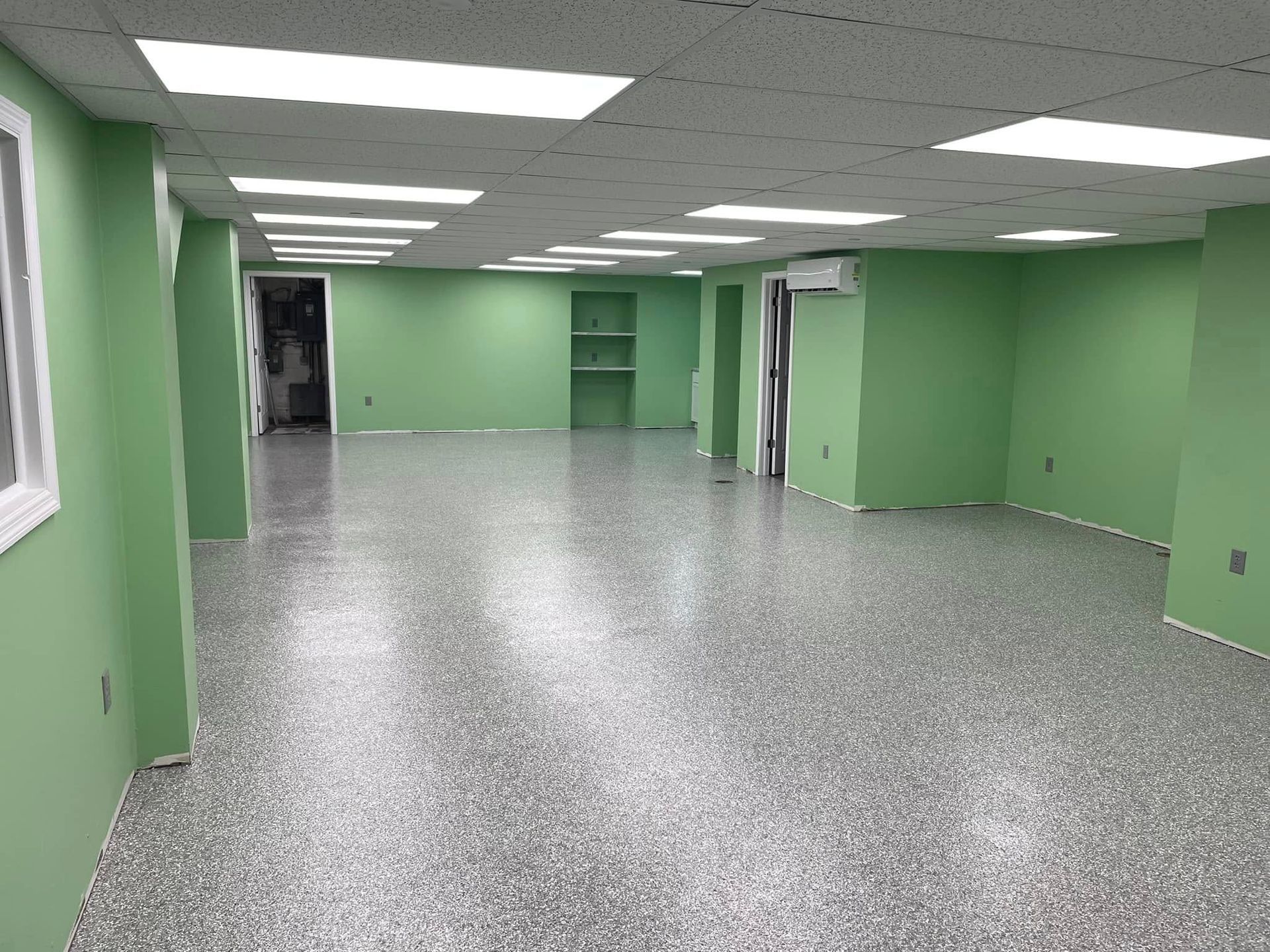 Empty room with green walls, gray speckled floor, and ceiling lights.