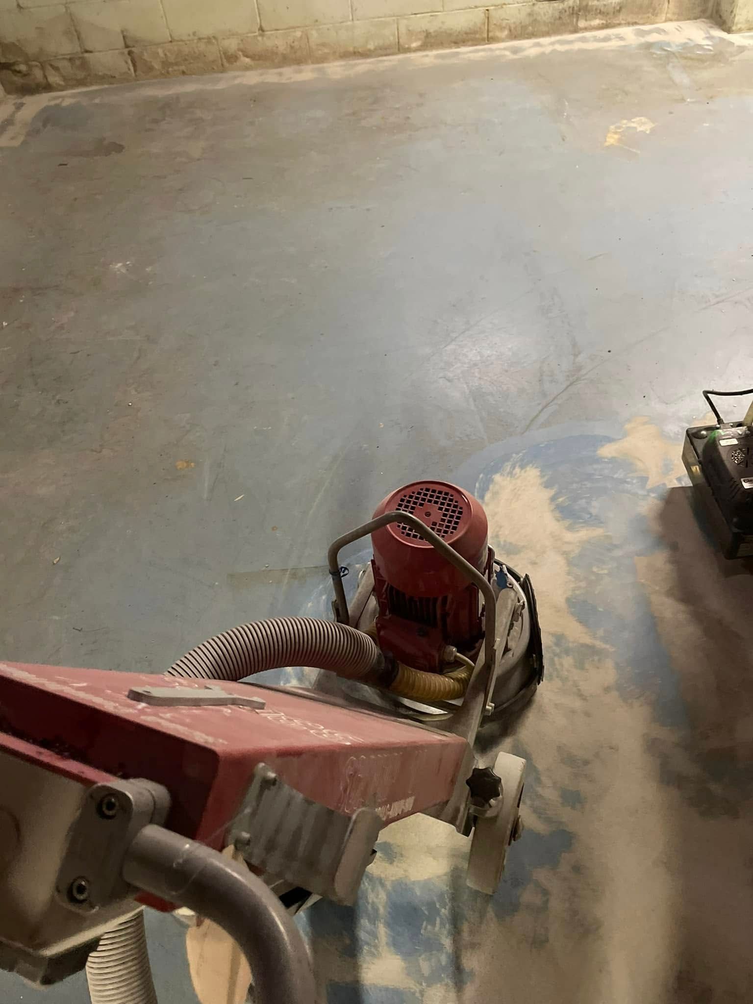 Floor grinder sanding a concrete floor, generating dust in an indoor setting.