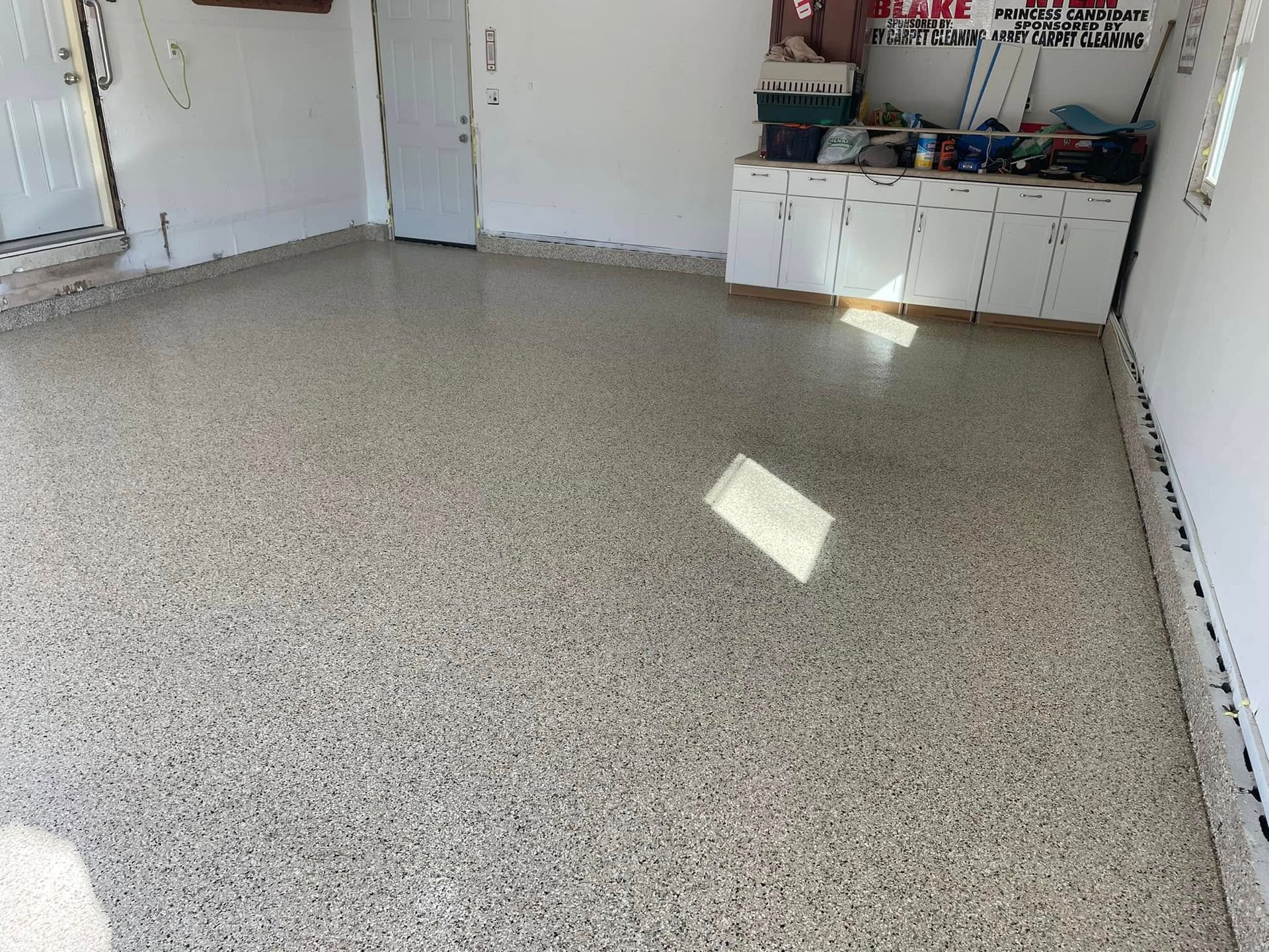 Garage interior with a speckled epoxy floor. White cabinets and a closed door are visible.