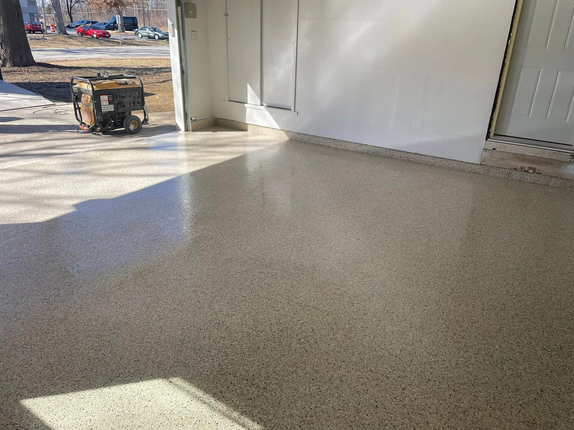 Shiny, speckled epoxy garage floor reflecting sunlight, with generator in the background.