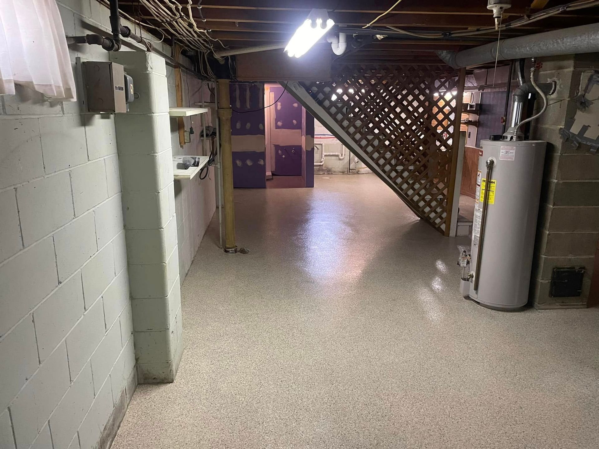 Basement with painted white brick walls, speckled floor, water heater, and wooden staircase.