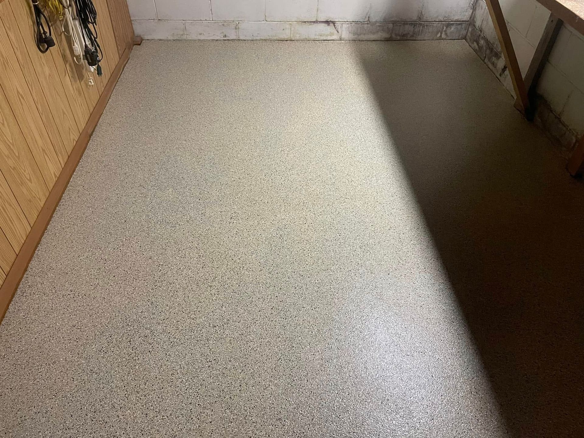 Gray speckled epoxy floor in a room with a wood-paneled wall and a white wall section.