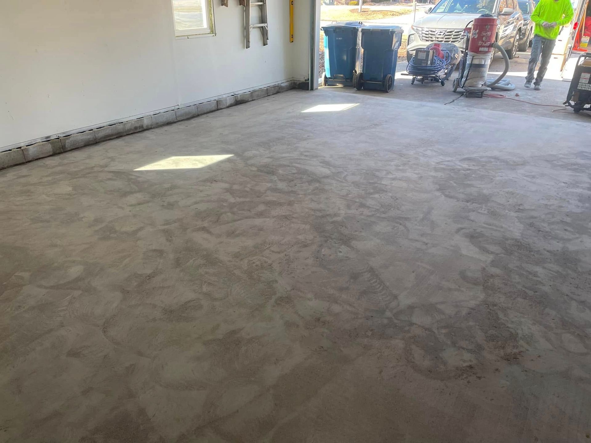 Concrete floor being ground, with construction equipment and workers visible.