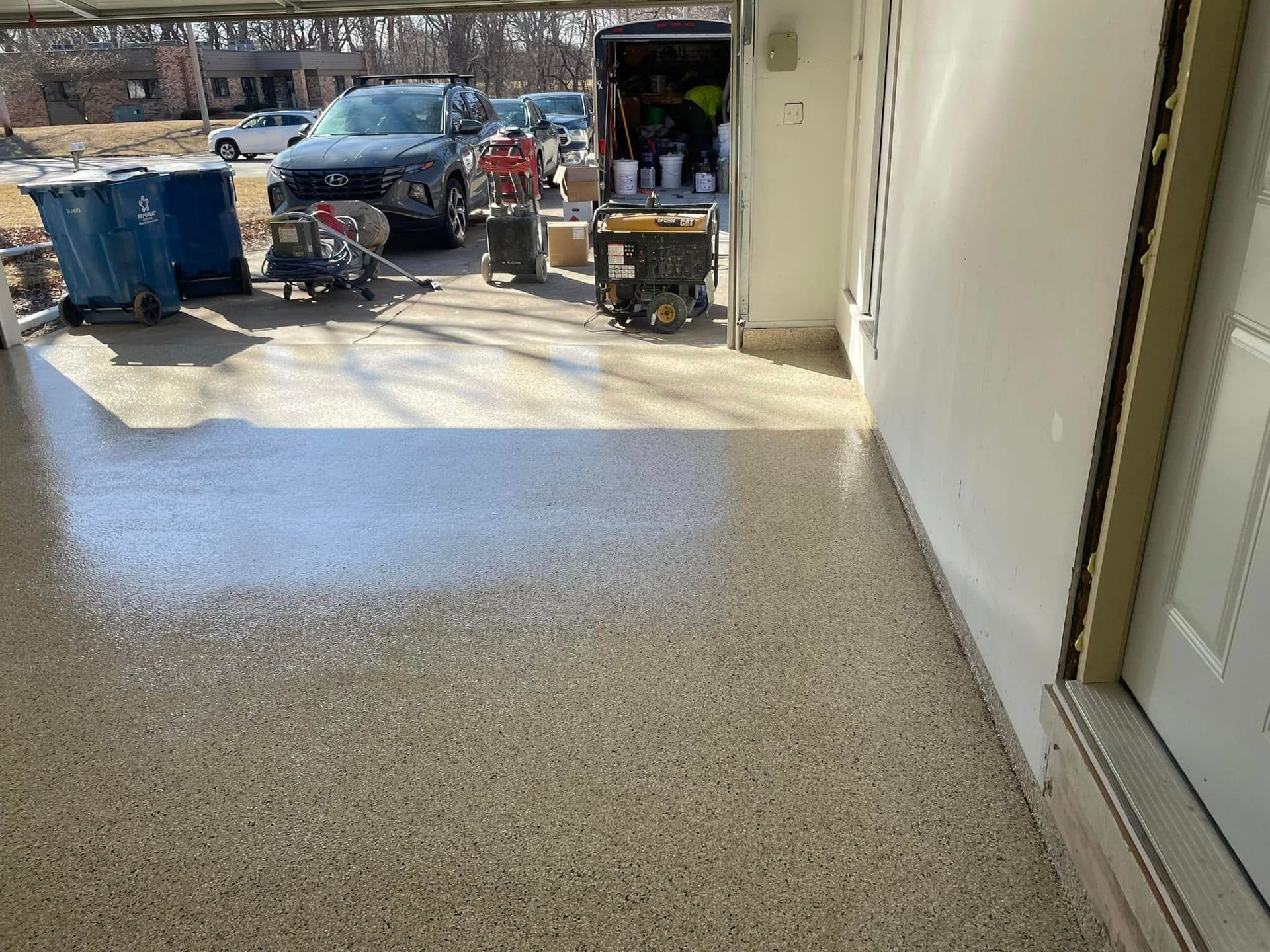 Garage with newly coated speckled floor; door open, equipment, and truck visible outside.