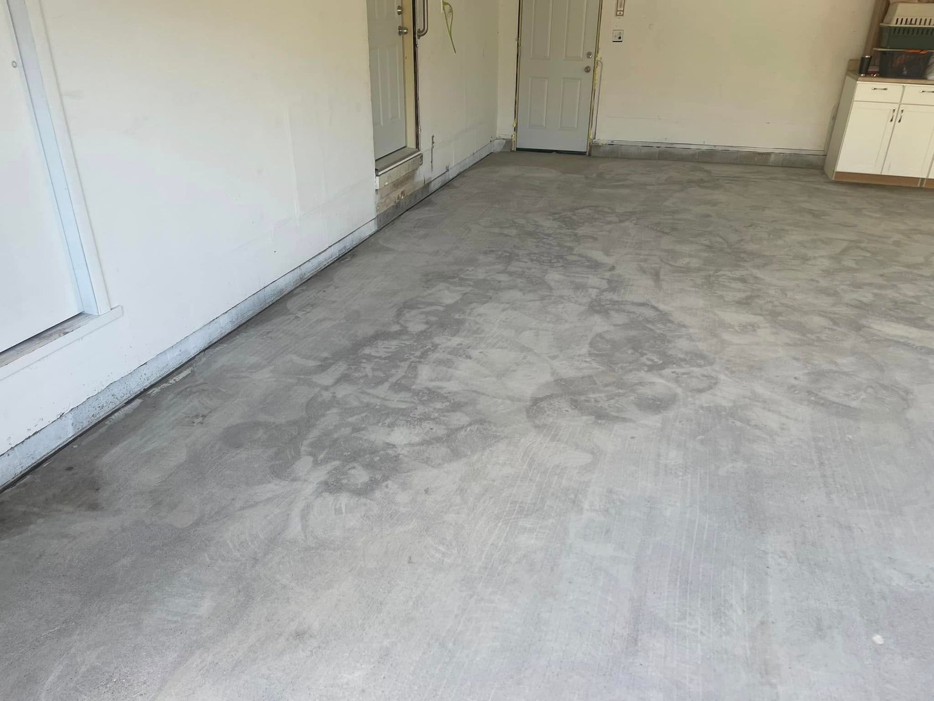 A concrete floor in a garage with patches of lighter gray and white walls.