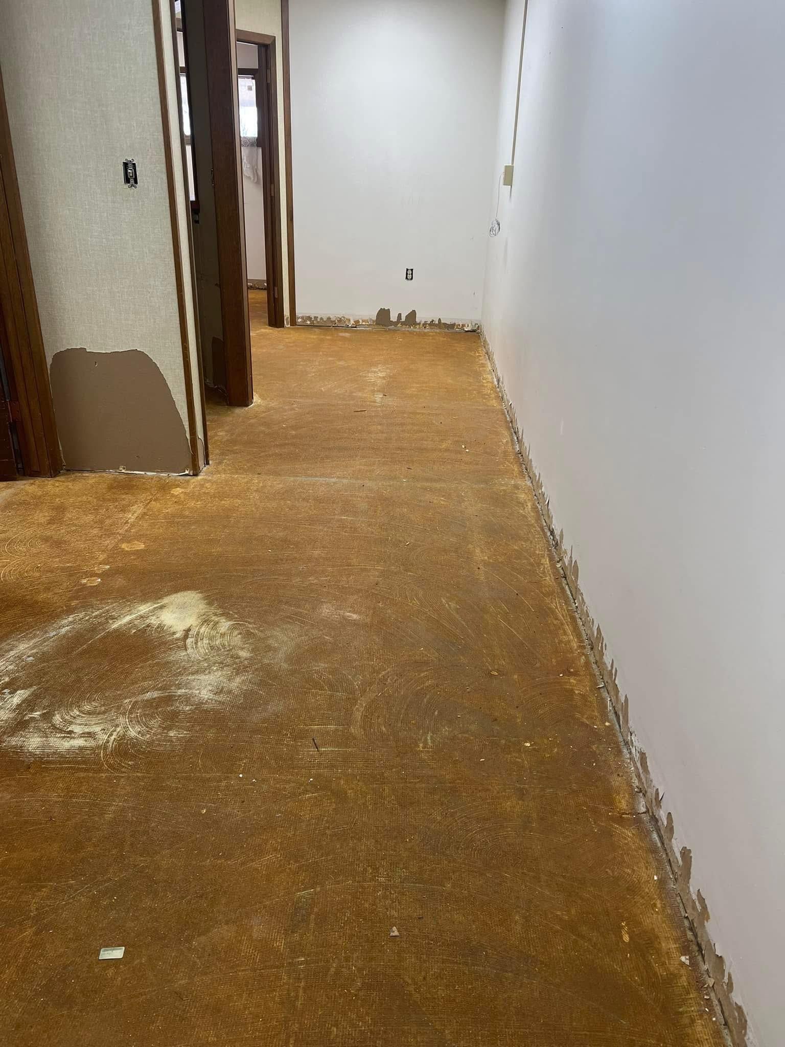 Hallway with exposed flooring and a white wall, under construction.