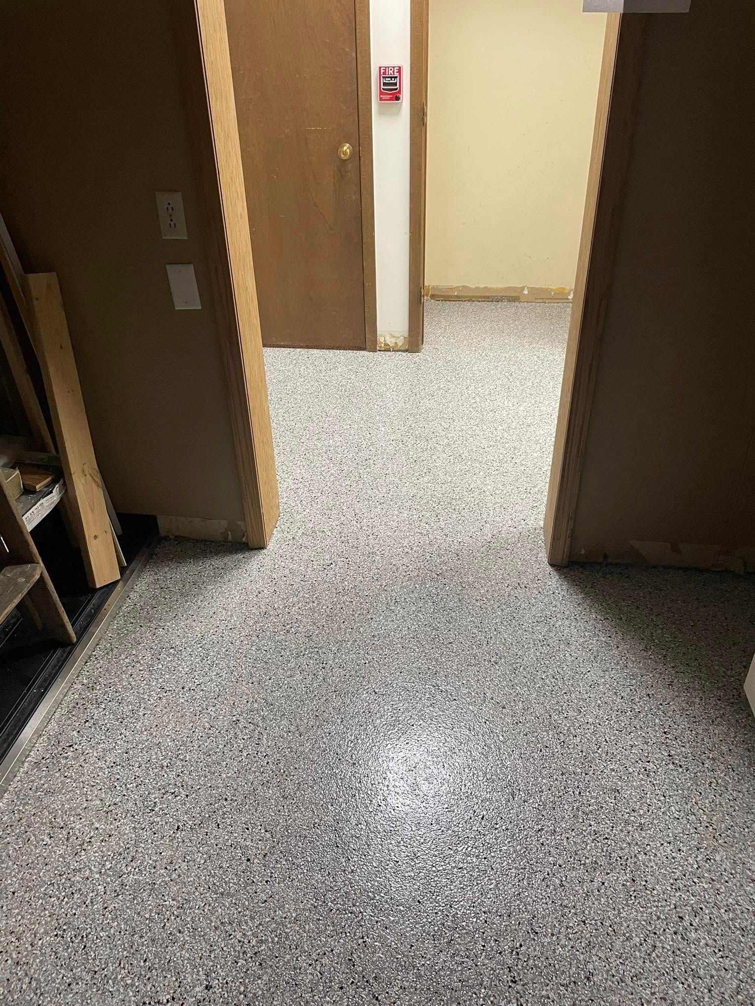Hallway with mottled gray flooring, two open doorways, and a closed door with a fire alarm.