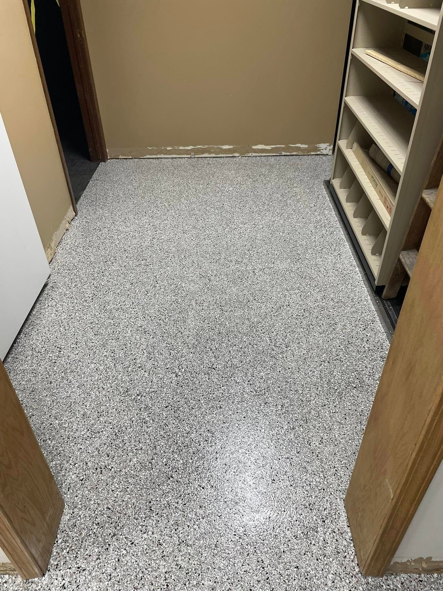 A room with a speckled gray and white epoxy floor; shelving unit on the right; doorway to the left.