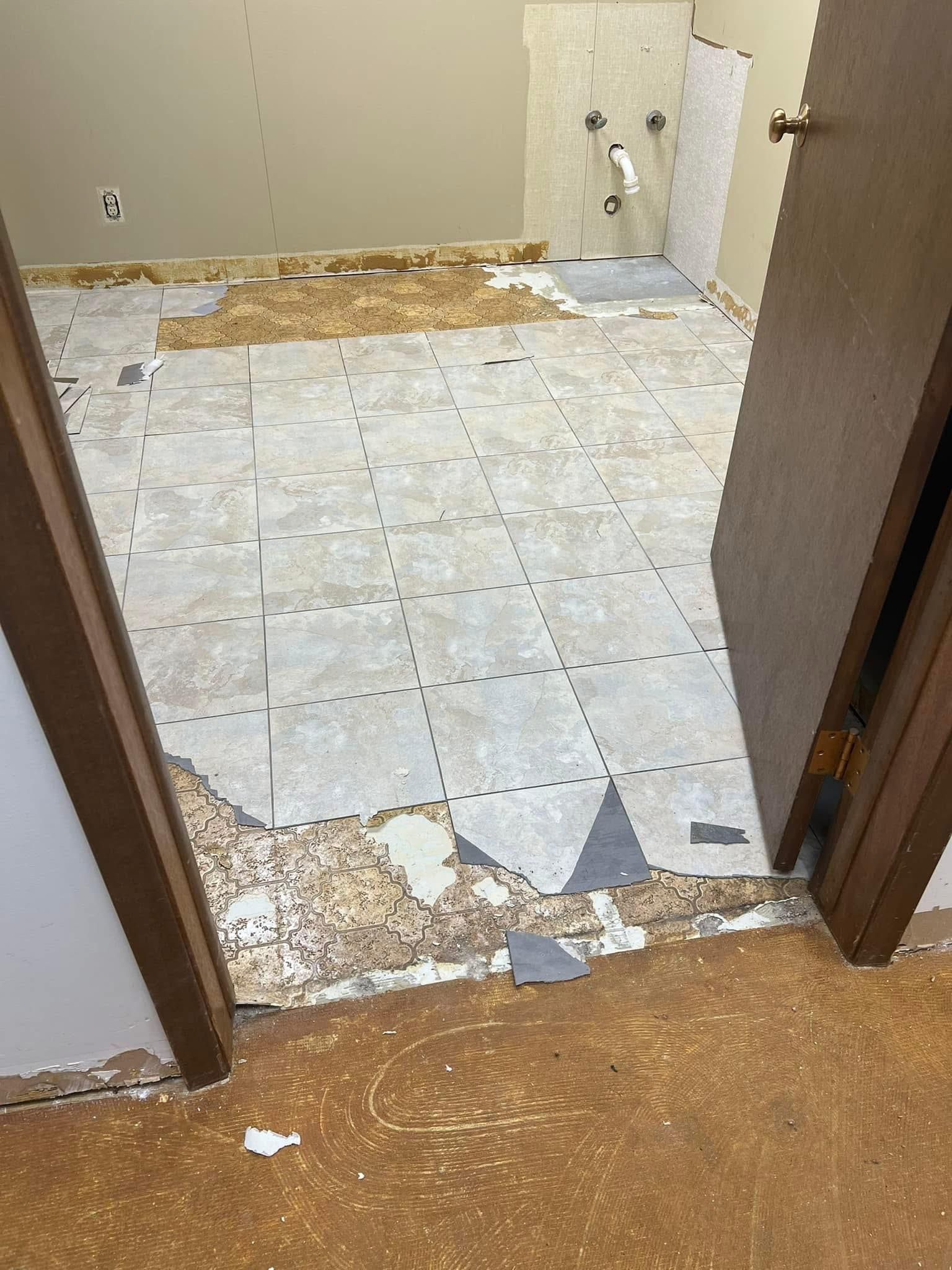 Room interior with damaged flooring; door frame in view. Light gray tiles are exposed.