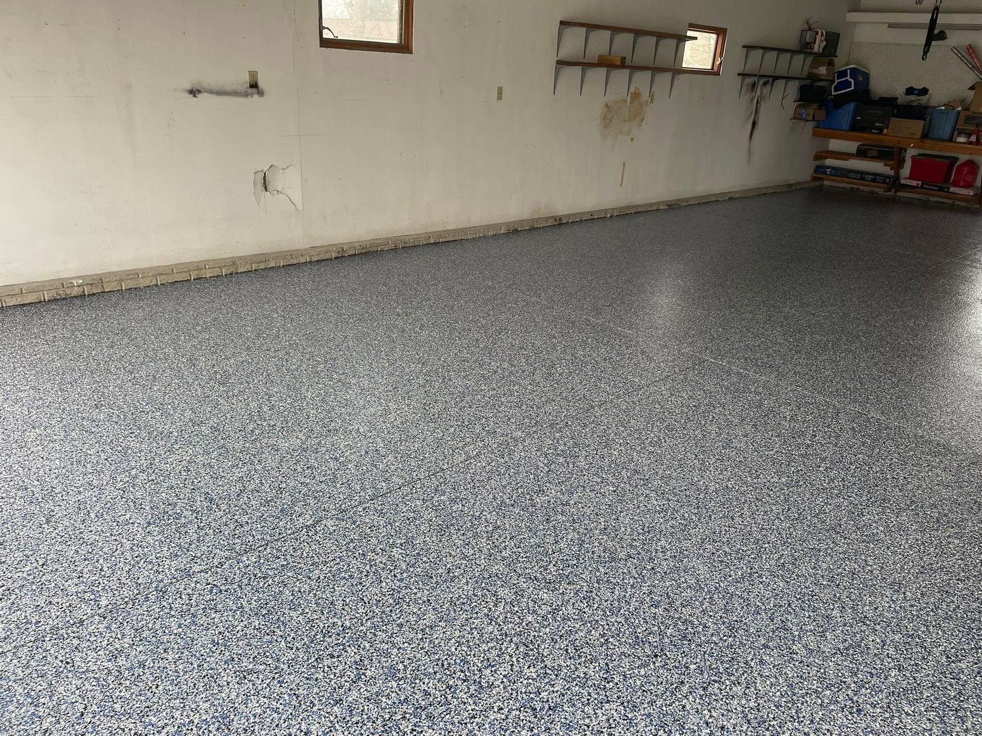 Garage with a speckled epoxy floor; walls are painted white, and there are small windows.