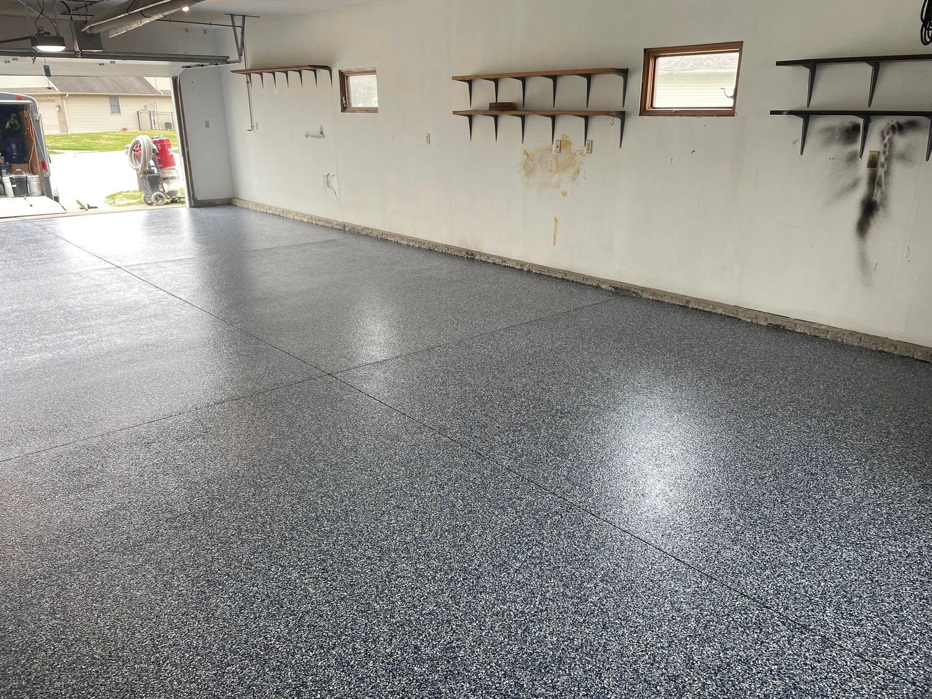 Garage with a gray and blue speckled epoxy floor. White walls, empty shelves.