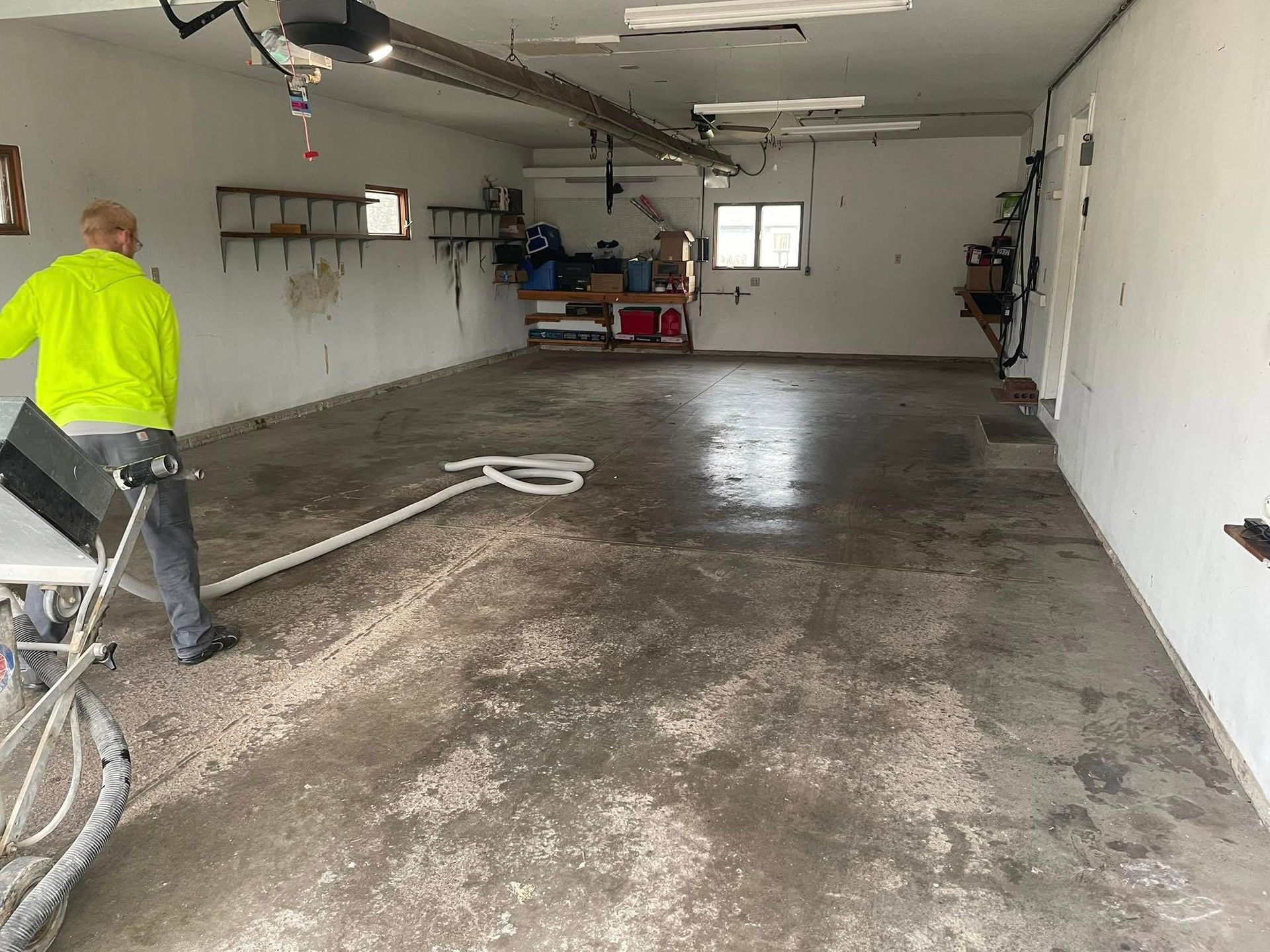 Person in bright clothing operating floor grinder in a garage. Concrete floor, garage door visible.