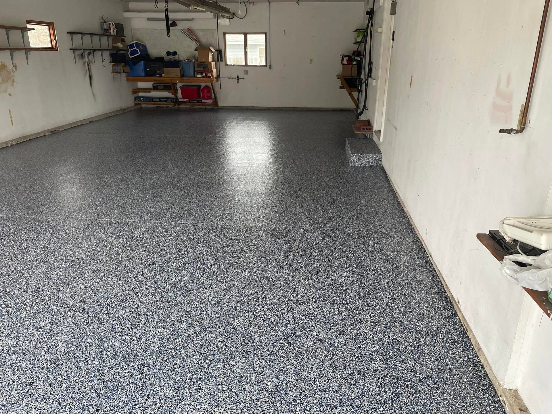 Garage with a speckled epoxy floor. White walls, storage shelves, and window in background.