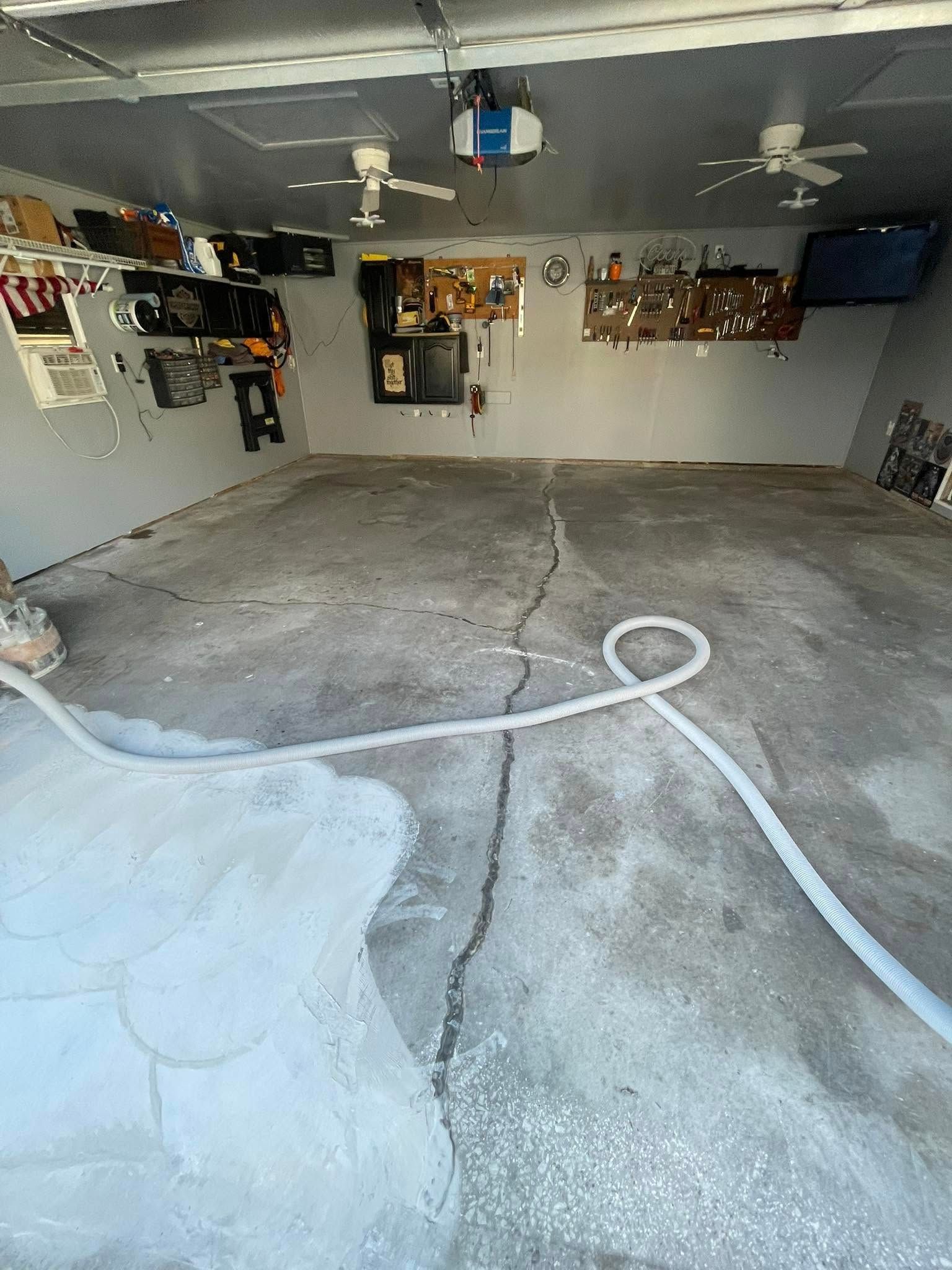 Garage interior with cracked concrete floor, tools on walls, hose on floor, and ceiling fans.