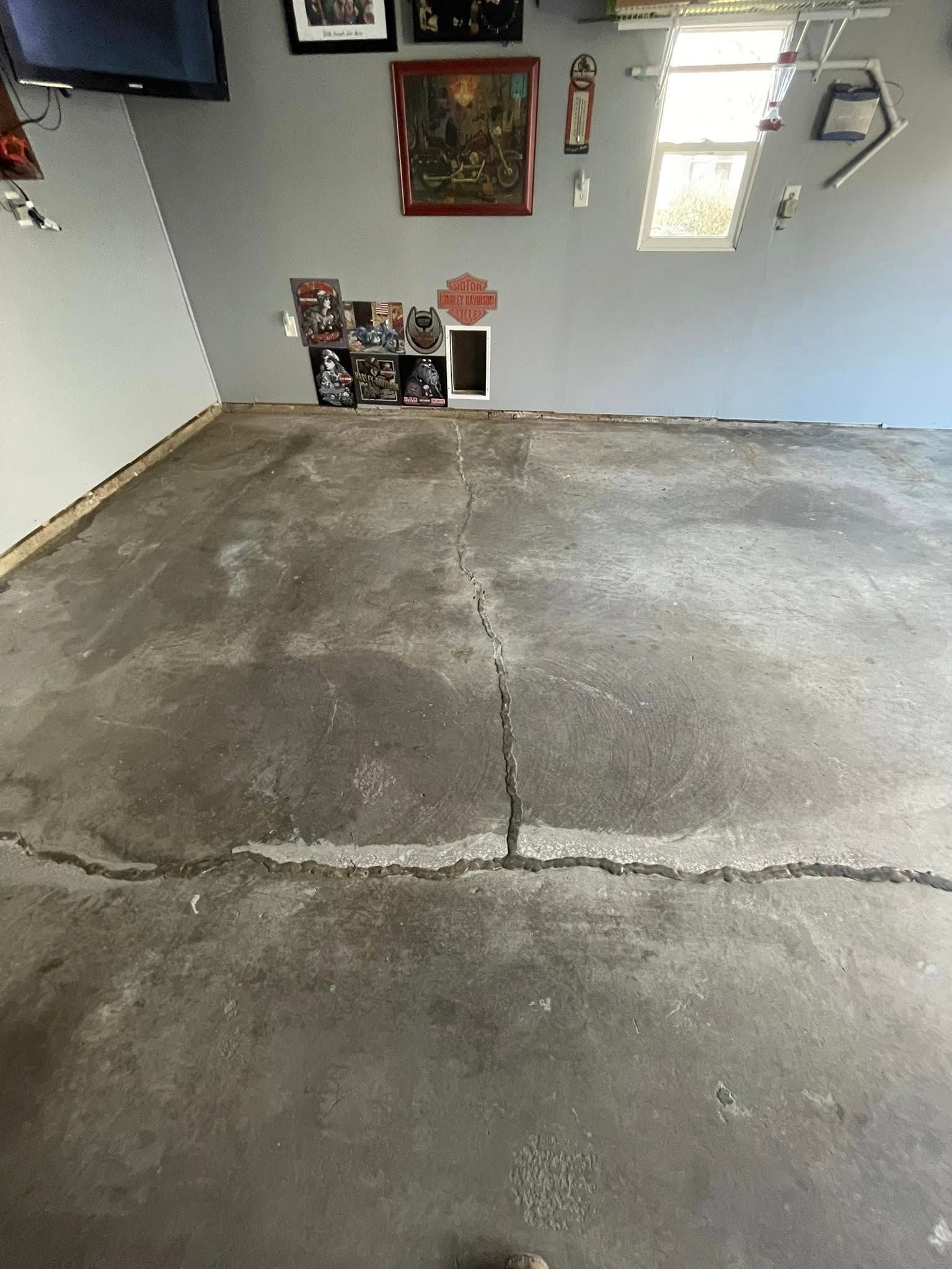Cracked concrete garage floor; gray walls with framed art, window, and small shelf.