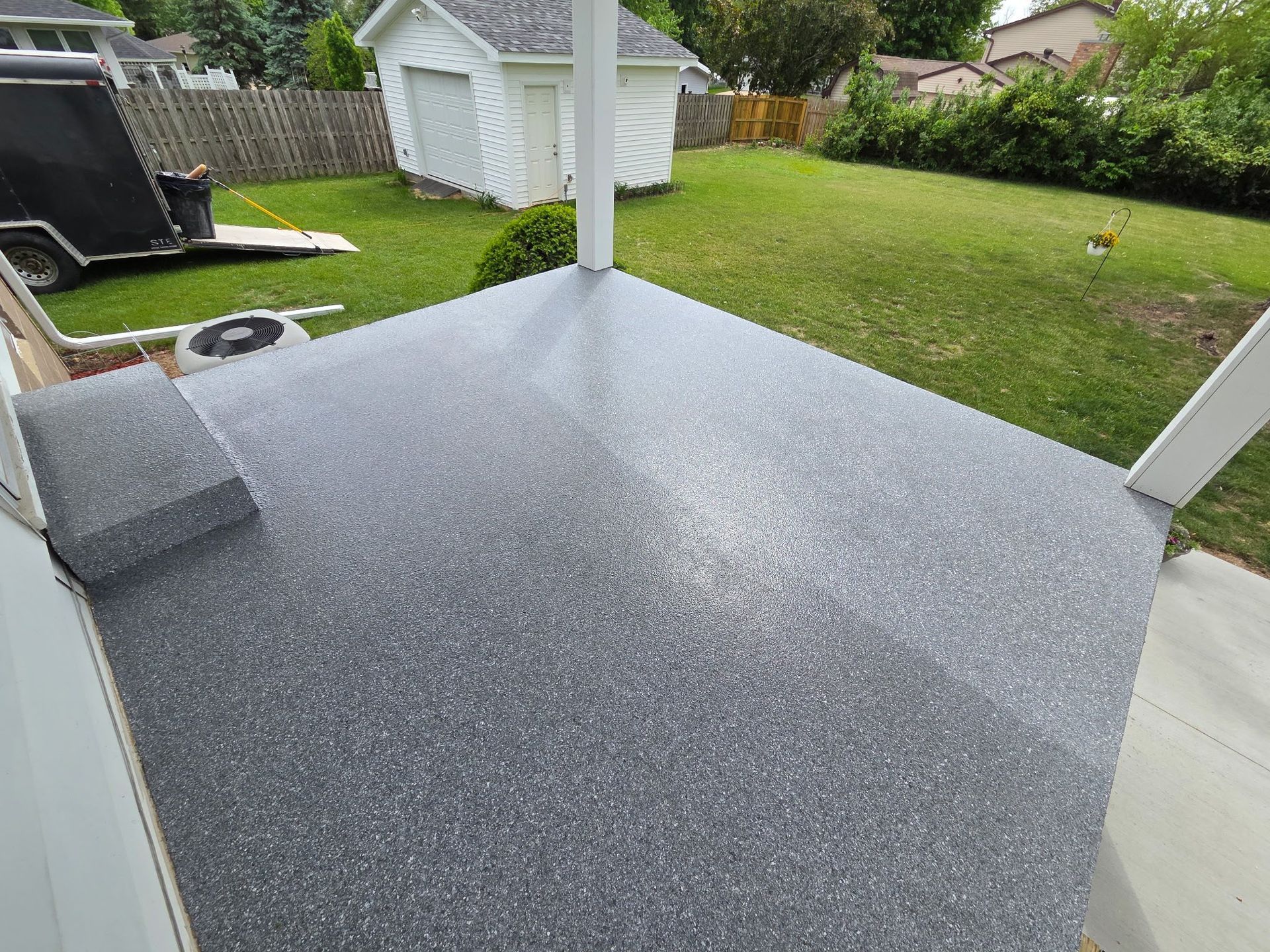 Gray speckled concrete patio with a small step, white columns, and a grassy backyard.