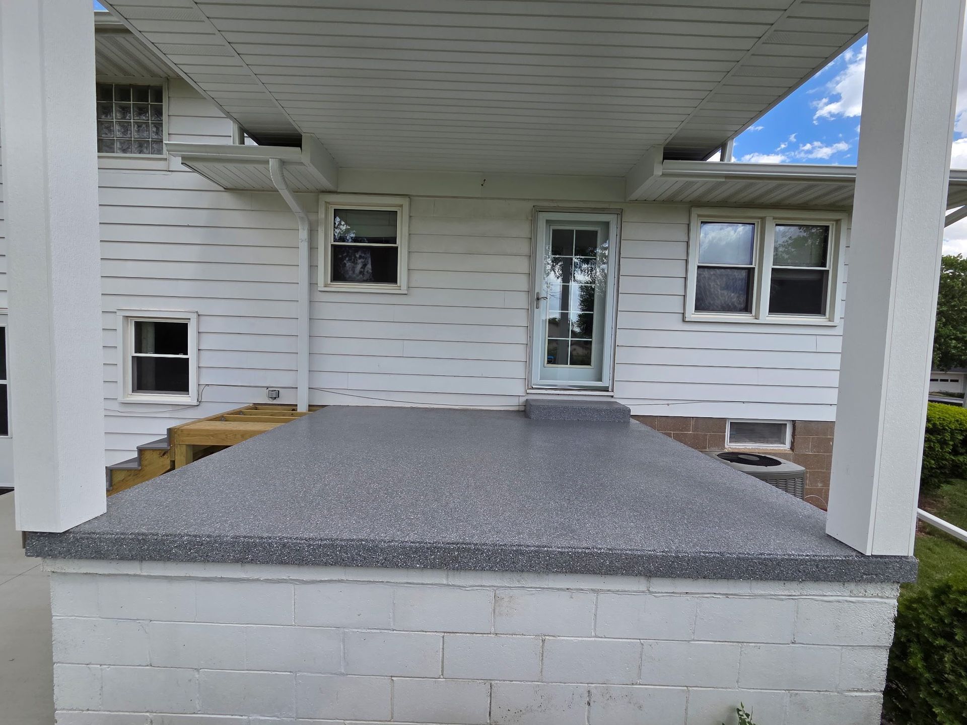 Gray concrete porch of a white house with a screen door and windows, beneath a white overhang.