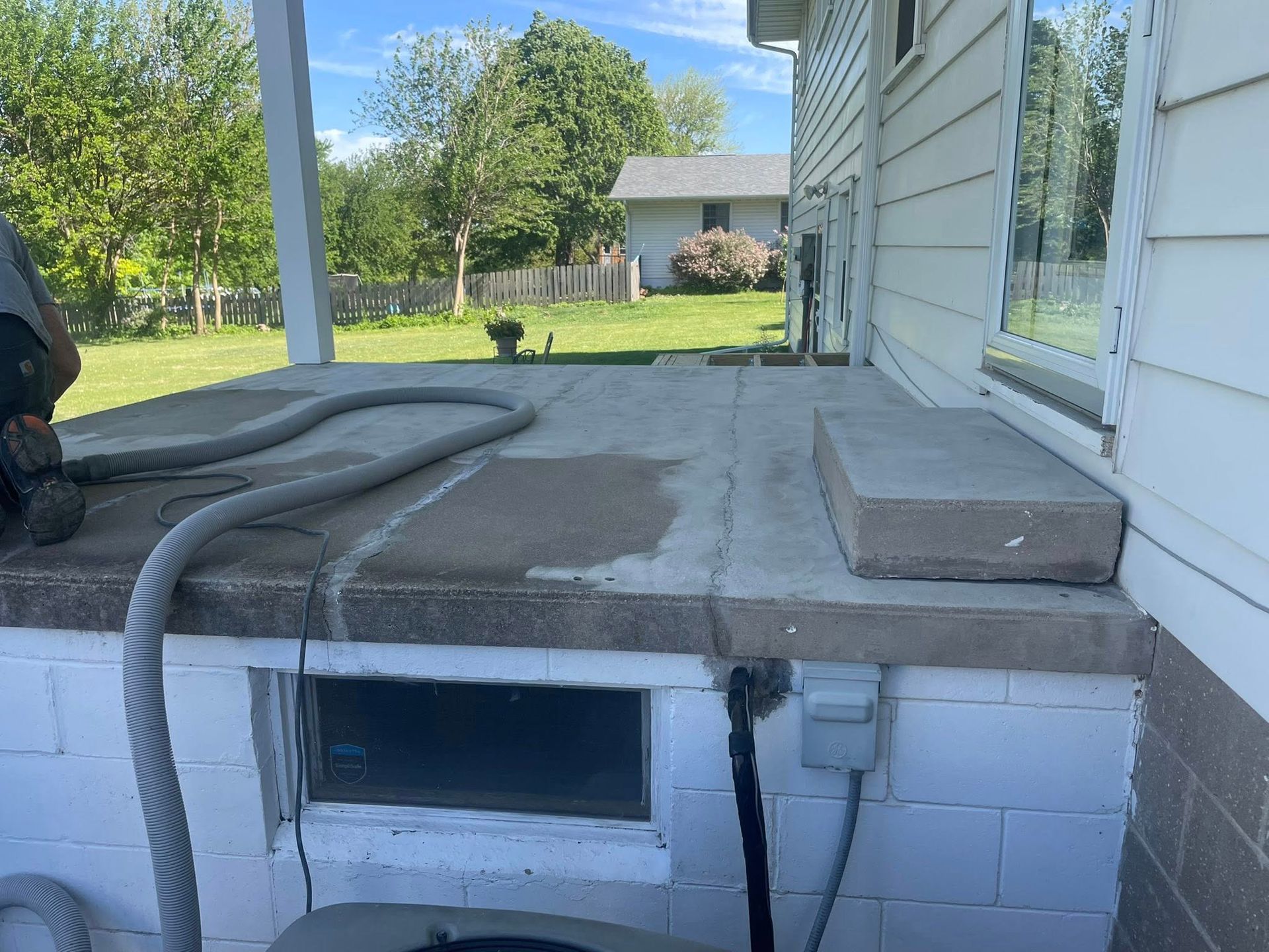 Concrete porch with a step, hose, and a window in brick foundation. White house exterior.