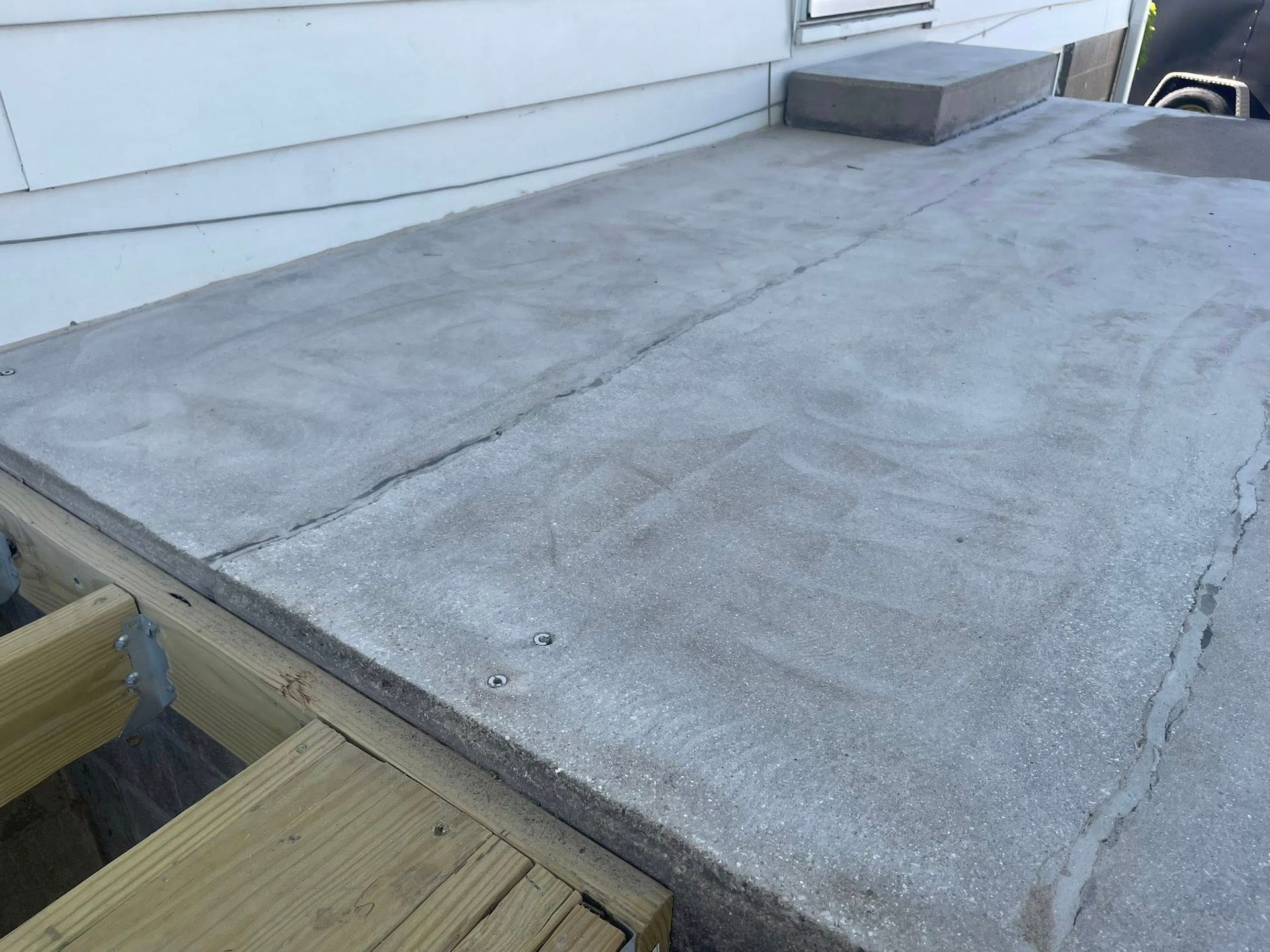 Concrete-covered deck surface with a small block on it, attached to a house with wooden framing.