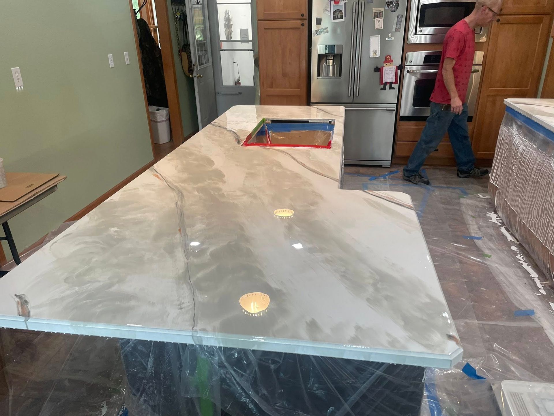 Kitchen with white and gray marbled countertop. Person walks by stainless steel appliances.