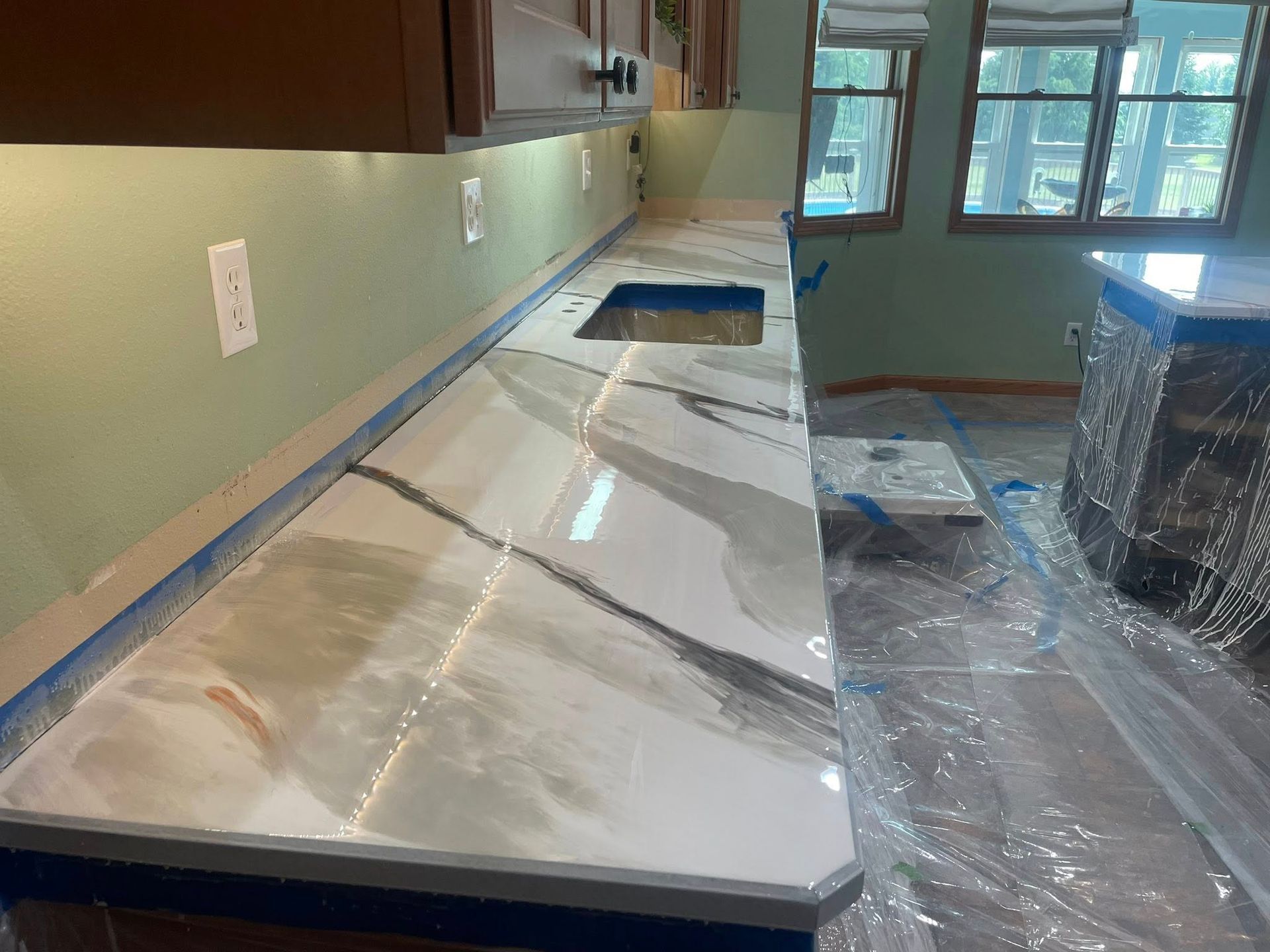 Kitchen with glossy white, gray and gold countertop. Sink cutout. Light green walls, brown cabinets.