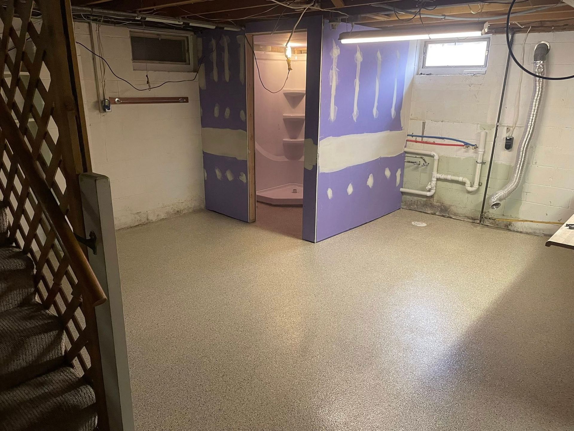 Basement renovation in progress; walls with purple drywall, unfinished shower stall, and speckled concrete floor.