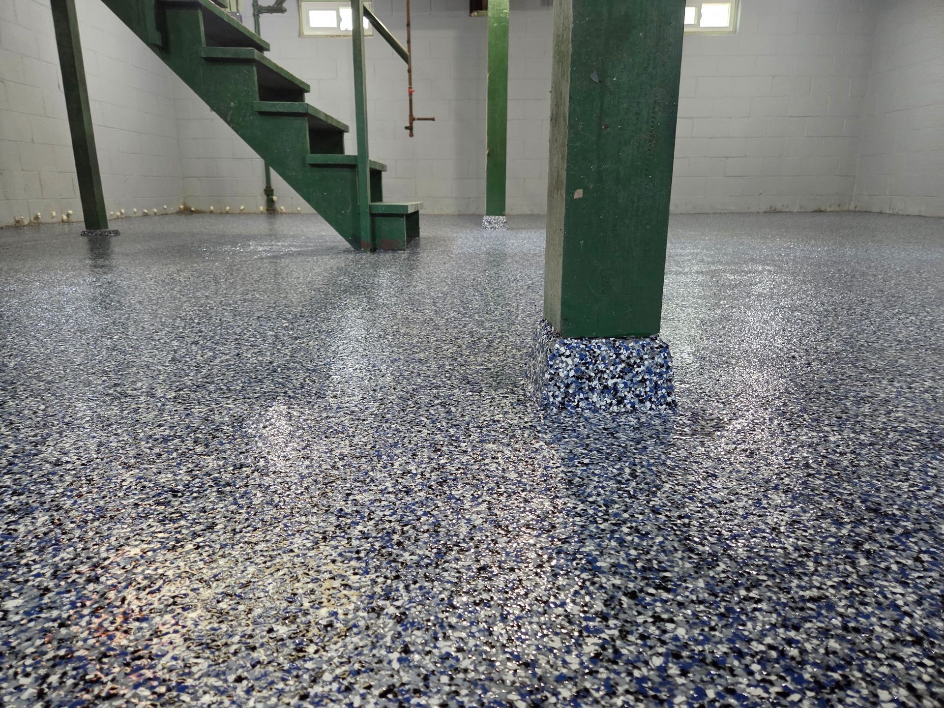Epoxy floor with blue, gray, and white chips in a basement, with green support beams and stairs.