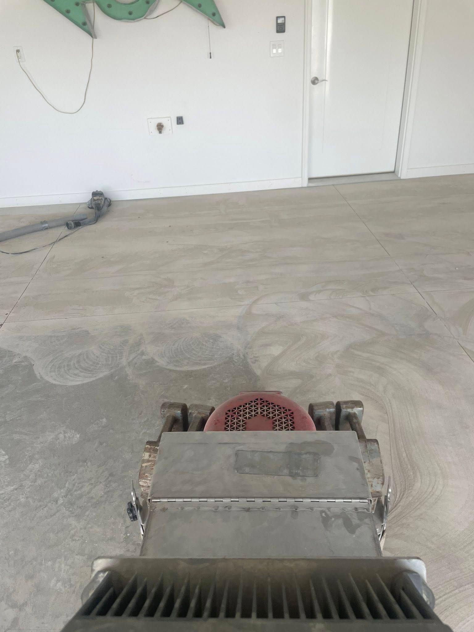 A floor grinder smoothing a concrete floor in a room with white walls and a doorway.