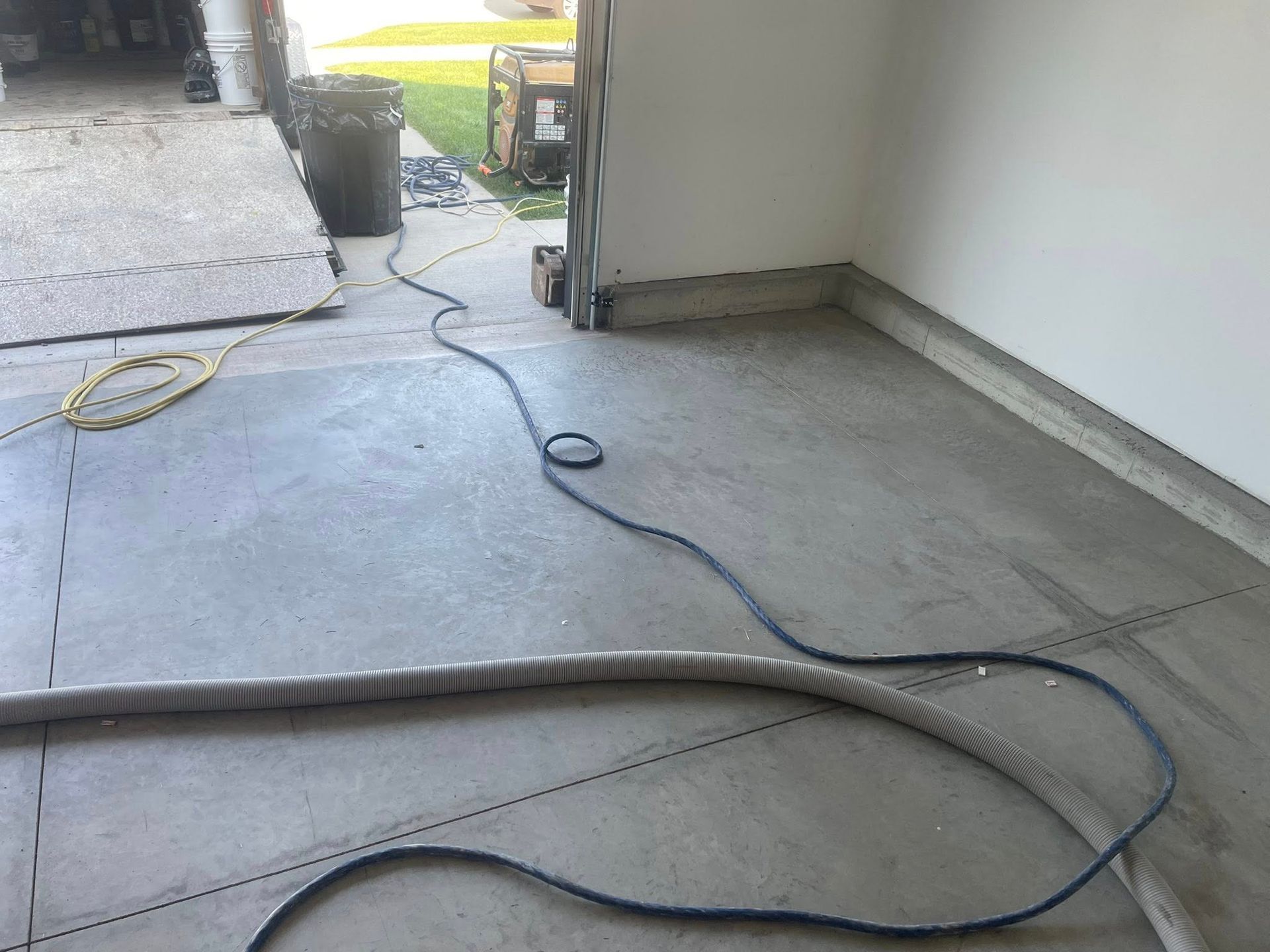 Concrete garage floor with hoses and electrical cords extending from open doorway.