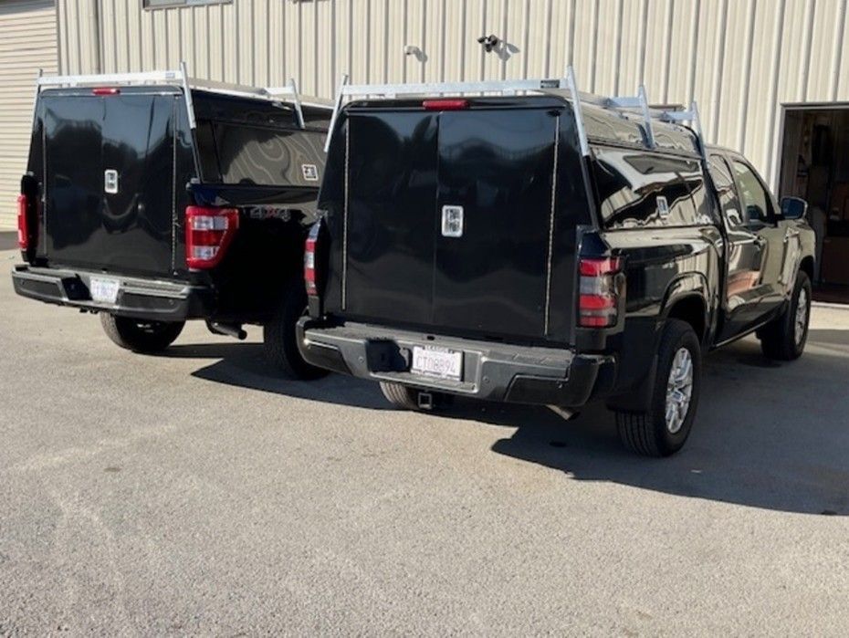Two black pickup trucks with enclosed storage units parked in front of a building.