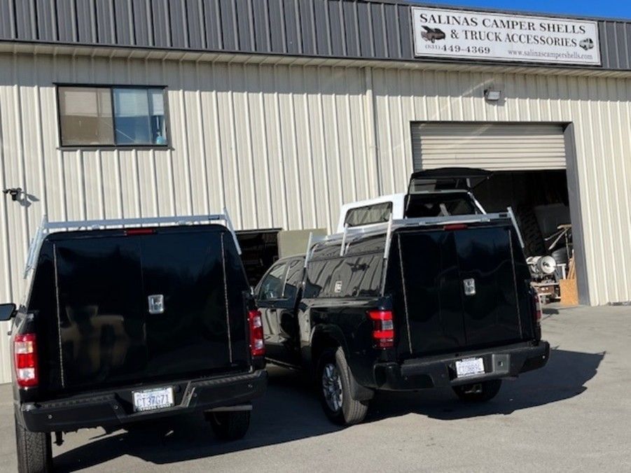 Two black pickup trucks with camper shells parked in front of a business, 
