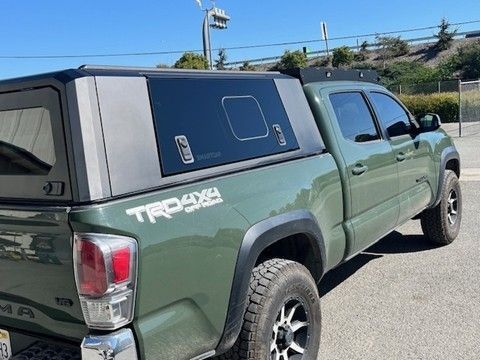 Green pickup truck with a black camper shell, parked outdoors.