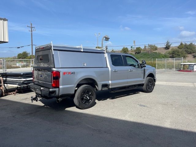 A silver Ford F-Series crew cab pickup truck with a matching utility cap parked in a lot on a sunny day.