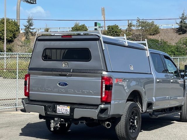 A gray Ford Super Duty pickup truck with a utility camper shell and ladder rack parked in an outdoor lot.