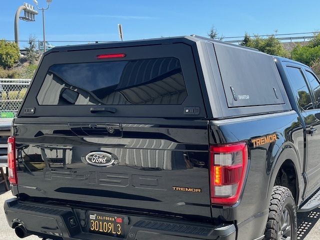 Black Ford F-150 Tremor pickup truck with a matching black camper shell, parked on a sunny day.