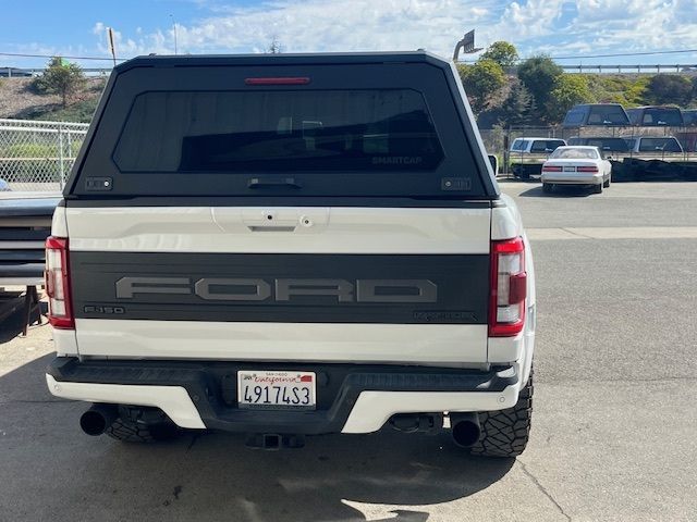 White Ford pickup truck with a black camper shell parked outdoors on a sunny day.