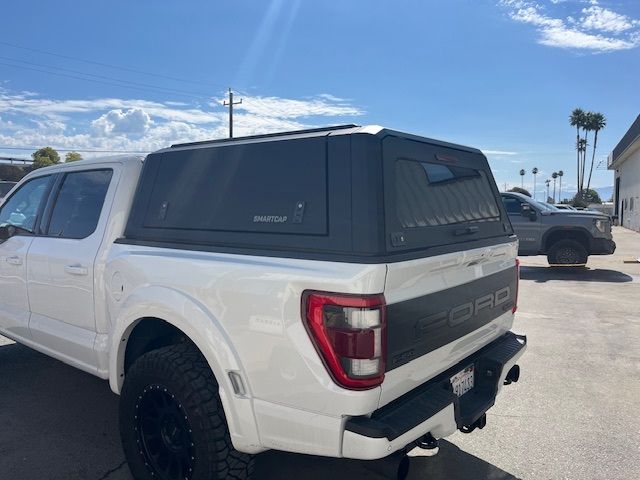 A white pickup truck with a black camper shell parked on a sunny lot, viewed from the rear passenger side.