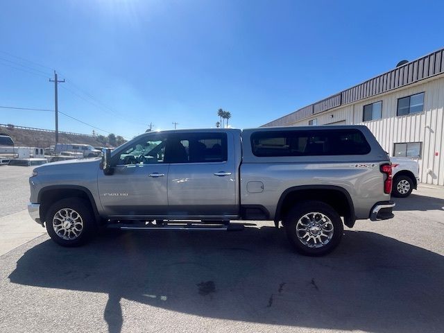 A silver crew cab pickup truck with a matching camper shell parked in a paved lot on a sunny day.