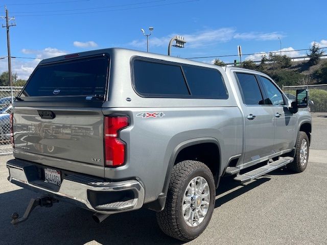 A silver Chevrolet pickup truck with a camper shell parked in a lot under a clear blue sky.