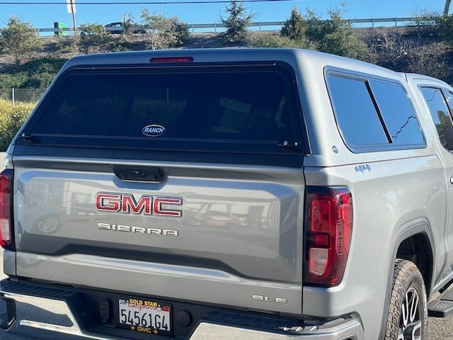 Rear view of a silver GMC Sierra pickup truck with a matching canopy, parked outdoors on a sunny day.